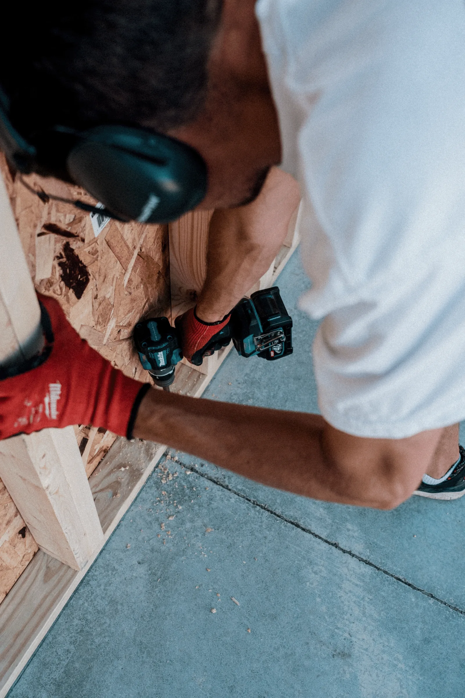 Overhead view of person wearing safety gear and red gloves working with wooden materials on a concrete surface.