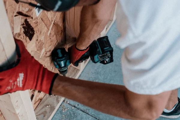 Person wearing safety gear and red gloves holds wooden plank during construction work on tiled floor.